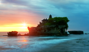 TANAH LOT TEMPLE. Tanah Lot stands on a rock some distance from the shore, towering over the sea. It is the most popular temple in Bali. Access to the temple is limited to low tide; even so, this picturesque temple is barraged by visitors. The temple's construction was supposedly inspired by the priest Nirartha in the 15th century; after spending the night on the rock outcrop where the temple now stands, he instructed local fishermen to build a temple on that site. Today, Tanah Lot is regarded as one of Bali's most important directional temples. A multimillion-dollar restoration effort in the 1990s saved Tanah Lot from falling into the sea. 
